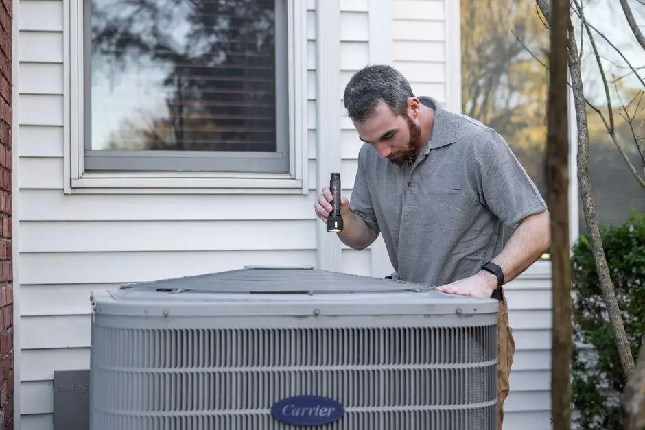 Technician inspecting outdoor air conditioning unit beside house with flashlight