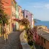 Traveler walking along cobblestone path beside colorful buildings and sea view in coastal village