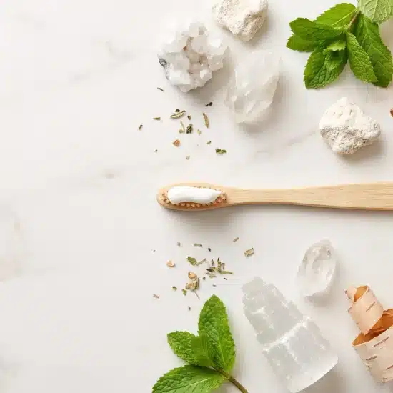 Bamboo toothbrush with toothpaste surrounded by mint leaves and natural stones on marble surface