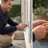 Man installing a gold lock on patio door in sunlit garden setting